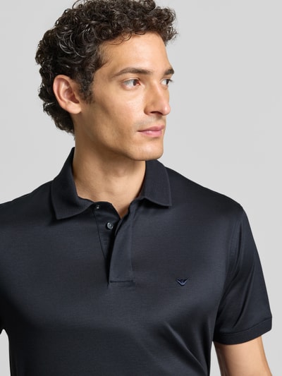Männermodel trägt Slim Fit Poloshirt mit Logo-Stitching von Emporio Armani in Dunkelblau, glatte Textur, Nahaufnahme Oberkörper.