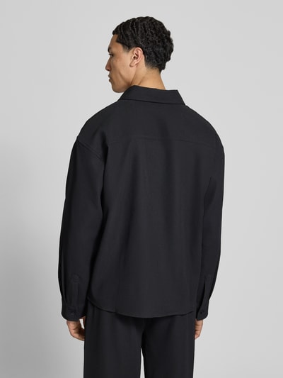 Męski model nosi Regular Fit Freizeithemd mit Kentkragen und Label-Stitching od Pegador, czarny materiał z domieszką stretchu, krój regular fit, długość tyłu w rozmiarze M: 68 cm, szerokość ramion w rozmiarze M: 50 cm, długość rękawa w rozmiarze M: 60 cm, widok całej sylwetki z tyłu.