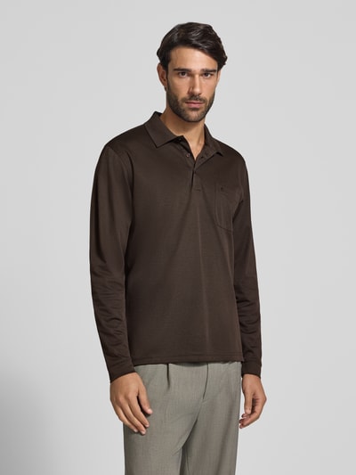 Męski model nosi Regular Fit Poloshirt aus Baumwoll-Mix od RAGMAN, brązowa koszulka polo z długim rękawem, kieszeń na piersi, elastyczne wykończenia, długość tyłu w rozmiarze M: 70 cm, zdjęcie całej sylwetki z przodu.