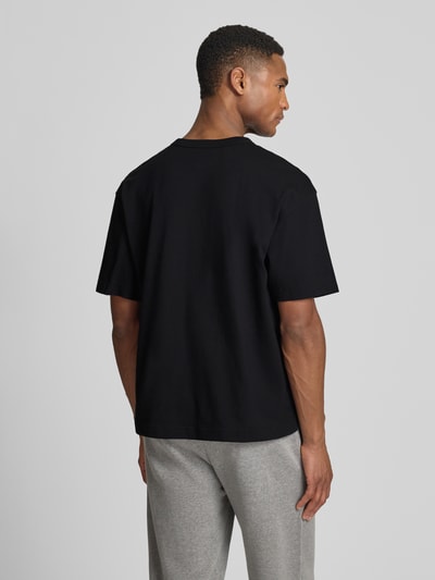 Männermodel trägt Cropped T-Shirt mit Rundhalsausschnitt von GAP in Schwarz aus reiner Baumwolle, Rückenlänge 63 cm, Ganzkörperansicht Rückansicht.
