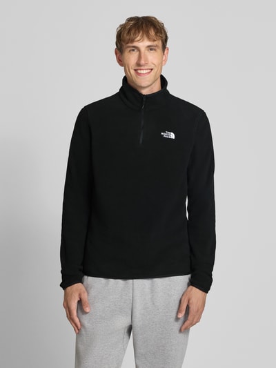 Mężczyznamodel nosi czarny sweter z polaru z kołnierzem zapinanym The North Face, Model 'GLACIER', prosty krój, wyhaftowane logo, Długość tyłu w rozmiarze M: 70 cm, Długość rękawów w rozmiarze M: 73 cm, ujęcie całej sylwetki od przodu.