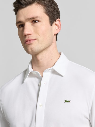Männermodel trägt Slim Fit Freizeithemd aus reiner Baumwolle von Lacoste, Optik: Unifarben, Kentkragen, Logo-Stitching, Nahaufnahme Oberkörper.