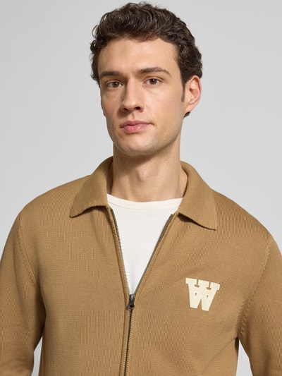 Mężczyzna nosi Regular Fit Cardigan in Strick-Optik Modell 'Tay' od Wood Wood z czystej bawełny, z zamkiem, kołnierzem i logo, krój regular fit; zbliżenie na górną część ciała.