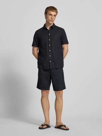 Männermodel trägt Slim Fit Leinenhemd mit Viskose-Anteil Modell 'Bobby' von Blend in Schwarz, Kentkragen, Kurzarm, Ganzkörperansicht von vorne.