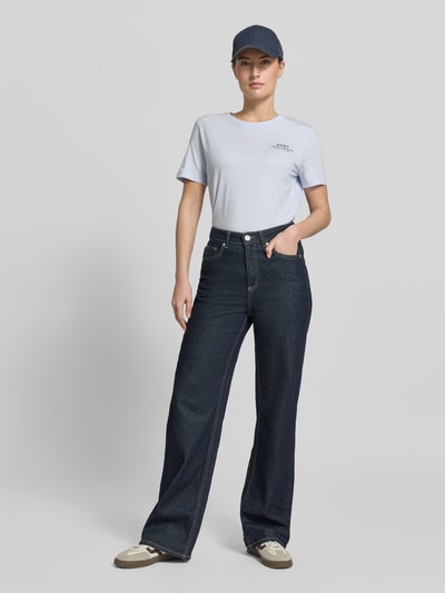 Vrouwenmodel draagt T-shirt met Label-Print en Rundhalsausschnitt van Gant in lichtblauw, puur katoen, regular fit, ruglengte maat S 57 cm, labelprint op borst, ronde hals, combiné met donkerblauwe jeans en pet, geheellichaamsaanzicht van voren.