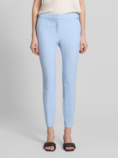 Frauenmodel trägt Slim Fit Hose mit Bügelfalten Modell 'HAGONIA-1' von HUGO in Hellblau, mit Logo-Applikation und Eingrifftaschen, Ganzkörperansicht von vorne.