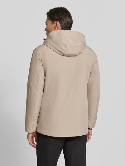Męski model nosi Regular Fit Jacke mit Logo-Print von Lindbergh z elastycznej mieszanki materiałów, beżowy kolor, kaptur z tunelem, tył gładki, długość tyłu w rozmiarze M: 74 cm, szerokość ramion w rozmiarze M: 46 cm, szerokość w klatce piersiowej w rozmiarze M: 42 cm, długość rękawów w rozmiarze M: 62 cm, widok całej sylwetki z tyłu.