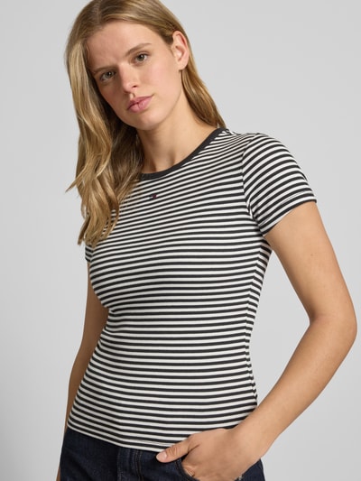 Frauenmodel trägt Slim Fit Damen T-Shirt aus Baumwoll-Mix mit Streifen, Logo-Stitching, Rundhals, Kurzarm von Tommy Jeans, Optik: Mehrfarbig, Ganzkörperansicht von vorne.