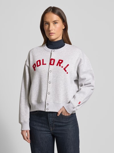 Frauenmodel trägt Sweatjacke mit Label-Print und Knopfleiste von Polo Ralph Lauren aus Baumwoll-Mix, Relaxed-Fit, grauer Grundton, Rundhalsausschnitt, Ganzkörperansicht von vorne.