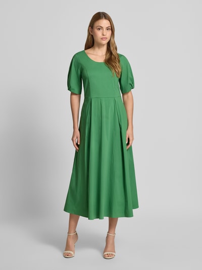 Vrouwenmodel draagt midi-jurk met plooien van More & More in groen katoenmix, getailleerde pasvorm, ronde hals, halflange mouwen, geheelbeeld vooraan. Ruglengte maat 36: 119 cm, borstwijdte: 44 cm, mouwlengte: 29 cm.