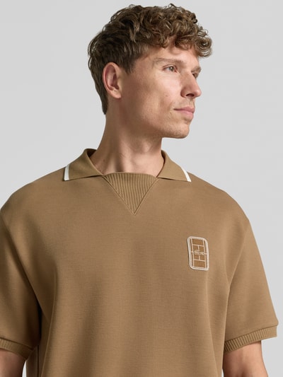 Männermodel trägt Loose Fit poloshirt van Lacoste in lichtbruin met witte details, fijne textuur, Nahaufnahme Oberkörper.