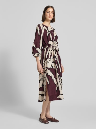 Frauenmodel trägt Midikleid aus Reinen Leinen mit floraler Allover-Print von Christian Berg Woman, dunkle und helle Kontraste, Ganzkörperansicht von vorne. Taillierte Passform, Rundhalsausschnitt, 3/4-Arm, Knopfleiste, Rückenlänge bei Größe 36: 122 cm, Brustweite: 50 cm, Ärmellänge: 45 cm.