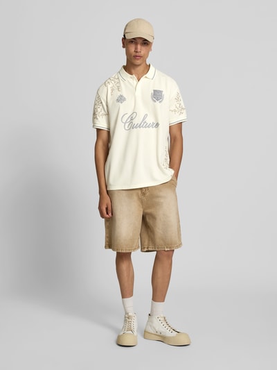Männermodel trägt Poloshirt floralem Allover-Stitching von Don’t Waste Culture in Creme mit Relaxed-Fit, Logo-Print und Polokragen, Ganzkörperansicht von vorne.