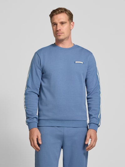 Männermodel trägt Sweatshirt mit Label-Patch und Rundhalsausschnitt von EA7 Emporio Armani aus Baumwoll-Mix in Blau, Loose-Fit, Ganzkörperansicht von vorne. Rückenlänge 67 cm, Ärmellänge 68 cm für Größe M.