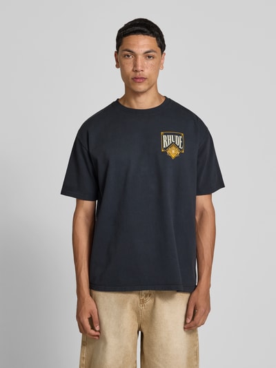 Männermodel trägt T-Shirt mit Label-Print von RHUDE, Herren T-Shirt aus reiner Baumwolle, gerader Schnitt, Rundhalsausschnitt, kurzärmeliges Design, Rückenlänge 71 cm, Größe M, Ganzkörperansicht von vorne.