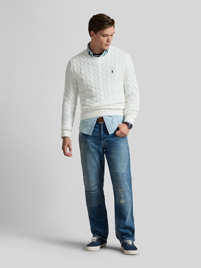 Männermodel trägt Regular Fit Strickpullover aus reiner Baumwolle von Polo Ralph Lauren, weiß, Zopfmuster, Logo, Ganzkörperansicht von vorne.
