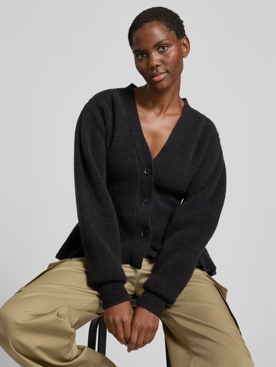 Frauenmodel trägt Relaxed Fit Cardigan aus Alpaka-Mix von ROTATE in Schwarz mit Strick-Optik, Volant-Saum und Knopfleiste, Nahaufnahme Oberkörper. Rückenlänge bei Größe S: 56 cm, elastischer Alpaka-Mix mit Woll-Anteil.