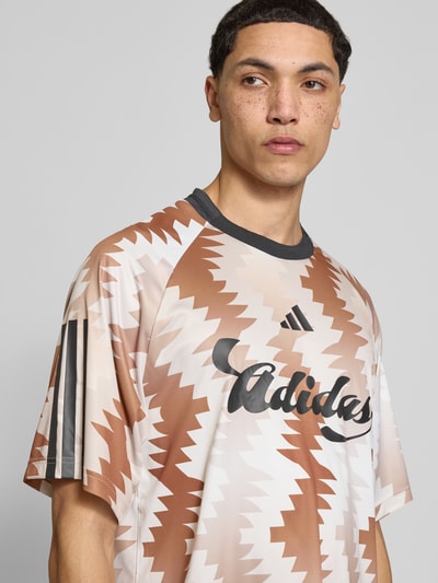 Männermodel trägt Regular Fit T-Shirt mit Allover-Muster von adidas Sportswear in Braun- und Beigetönen, Rundhals, Kurzarm, Label-Print, Nahaufnahme Oberkörper.