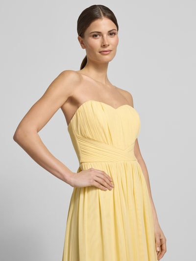 Frauenmodel trägt Cocktailkleid im Off-Shoulder-Look von Lipsy in Gelb, tailliert, fließendes Material mit Raffungen, Nahaufnahme Oberkörper.