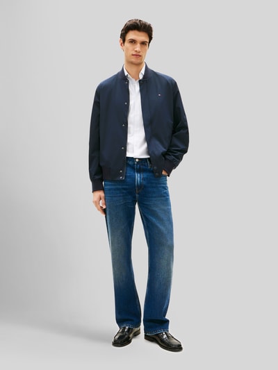 Männermodel trägt Regular Fit Blouson mit wasserabweisender Funktion von Tommy Hilfiger in Optik: Unifarben, Ganzkörperansicht von vorne. Passform: Regular-Fit, Kragenform: College-Kragen, Verschluss: Druckknopf- und Reißverschluss, Applikation: Logo-Stitching, Ärmelform: Langarm, Ärmelabschluss: Gerippt, Rumpfabschluss: Gerippt, Funktion: wasserabweisend, winddicht, Taschen: Innenreißverschlusstasche, seitliche Reißverschlusstasche.