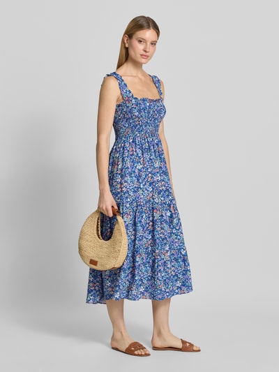 Modelka nosi Midikleid mit Smok-Details und Volantsaum von Apricot, niebieskie kwiaty, tkanina wiskozowa, krój taliowany, szerokie ramiączka, całopostaciowe ujęcie z przodu.