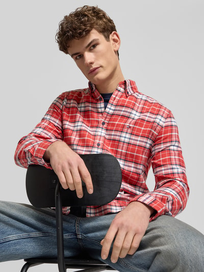 Mannelijk model draagt Regular Fit Flanellhemd aus reiner Baumwolle van Tommy Jeans met rood-wit-blauw ruitpatroon, flanellen structuur, button-down kraag, lange mouwen, logo-details, vooraanzicht borst opname.