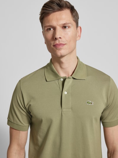 Männermodel trägt Regular Fit Poloshirt aus Baumwoll-Mix von Lacoste in Olivgrün, unifarben, Piqué-Struktur, Nahaufnahme Oberkörper.