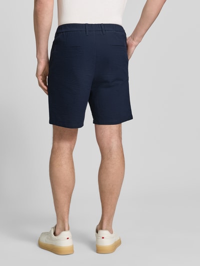 Męski model nosi Regular Fit Bermudas aus Baumwoll-Mix Modell 'KARL' von SELECTED HOMME, w paski, wpuszczane i tylne kieszenie, seersucker, kolor granatowy, mieszanka bawełny, efekt: wzór w paski, szlufki na pasek, zapięcie na guzik i ukryty zamek błyskawiczny, elastyczny pas, całkowity widok z tyłu.
