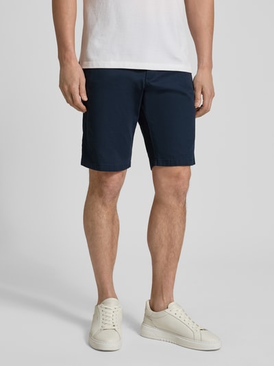Mężczyzna nosi Regular Fit Bermudas aus Baumwoll-Mix Modell 'PHOENIX' od s.Oliver RED LABEL, ciemnoniebieski twill, długość cropped, gładka tkanina, 5 kieszeni, pasek, zapięcie na guzik i ukryty zamek, widok całej sylwetki z przodu.
