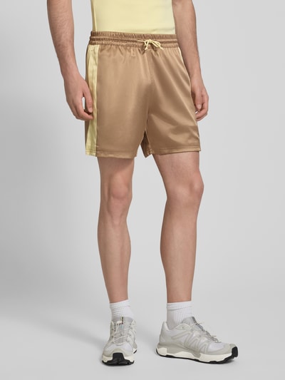 Männermodel trägt Shorts aus Satin mit Label-Stitching und elastischem Bund von BLKVIS, Regular-Fit, gold-beige, Ganzkörperansicht von vorne. Herren Shorts aus Satin mit Tunnelzug, Bundweite 42 cm, Innenbeinlänge 14 cm, Größe M.