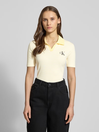Frauenmodel trägt Slim Fit Poloshirt mit Label-Stitching von Calvin Klein Jeans in Gelb, Ripp-Optik, V-Ausschnitt, Ganzkörperansicht von vorne.
