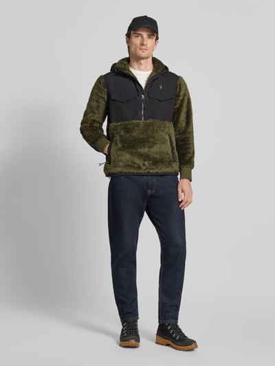 Männermodel trägt Fleecepullover mit Kapuze und Brusttaschen Modell 'CURLY' von Polo Ralph Lauren in Olivgrün und Schwarz, Ganzkörperansicht von vorne, Regular Fit, Label-Stitching, Reißverschlusstaschen.