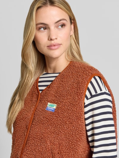 Frauenmodel trägt Relaxed Fit Weste aus Teddyfell Modell 'Hoktown' von American Vintage, braun, Logo-Patch, Nahaufnahme Oberkörper. Damen Weste aus Teddyfell, Knopfleiste, Gr. XS/S: Rückenlänge 56 cm, Schulterbreite 43 cm, Brustweite 63 cm.