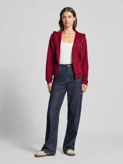 Frauenmodel trägt Regular Fit Sweatjacke aus Baumwoll-Mix von HUGO, dunkelrot, kombiniert mit blauer Hose, Ganzkörperansicht von vorne, damska bluza dresowa