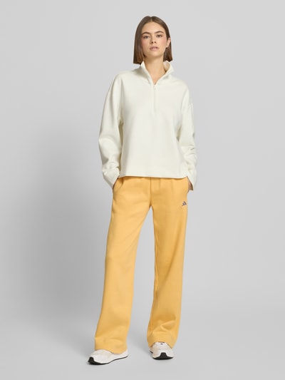 Kobiece modelka nosi Spodnie dresowe z logo i elastycznym pasem od adidas Sportswear, mieszanka bawełny, krój regular fit, tunel, długość wewnętrzna 79 cm, kolor żółty, widok całej sylwetki z przodu.