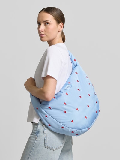 Kobiece model nosi Crossbody Bag mit Logo-Patch Modell 'Puffy' od STUDIO NOOS, jasnoniebieski z wyhaftowanym motywem na całej powierzchni, główna przegroda z zamkiem błyskawicznym, pasek na ramię, naszywka z logo; szerokość w rozmiarze 1: 47 cm, długość w rozmiarze 1: 34 cm, głębokość w rozmiarze 1: 10 cm, długość paska na ramię w rozmiarze 1: 72 cm; zdjęcie całej sylwetki z przodu.