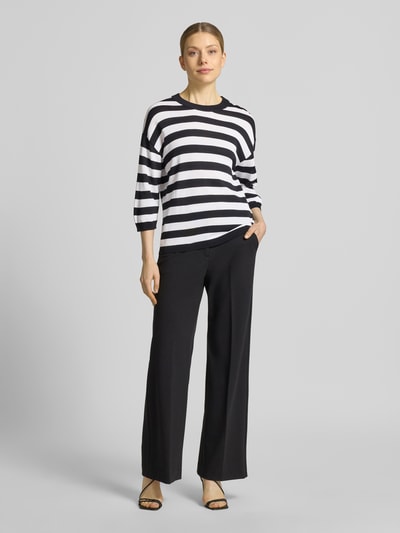 Frauenmodel trägt schwarz-weiß gestreiftes Regular-Fit Oberteil aus Viskose-Mix Modell 'Lani' von GUIDO MARIA KRETSCHMER WOMAN, Strick-Optik, 3/4-Arm, Rundhalsausschnitt, elastische Ärmelabschlüsse, kombiniert mit schwarzer Hose, weiche Textur. Ganzkörperansicht von vorne.