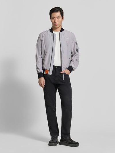 Männermodel trägt Bomberjacke mit Label-Patch und Eingrifftaschen von Original Bombers in Grau mit Reißverschluss, Gerader-Schnitt, Ganzkörperansicht von vorne, Kontext: Herren Bomberjacke, Reißverschlusstasche am Ärmel, Druckknopfverschluss, Gerippte-Abschlüsse, Rückenlänge 67 cm, Schulterbreite 43 cm, Brustweite 53 cm, Ärmellänge 68 cm.
