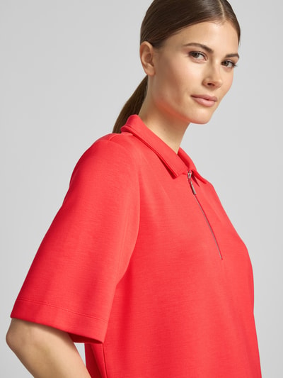 Modelka kobieca nosi Regular Fit Poloshirt mit Reißverschluss von Christian Berg Woman, mieszanka materiałów z domieszką modalu, rękaw o dł. 1/2, kolor intensywnej czerwieni, gładka tekstura, zamek błyskawiczny, półzbliżenie na górną część ciała.
