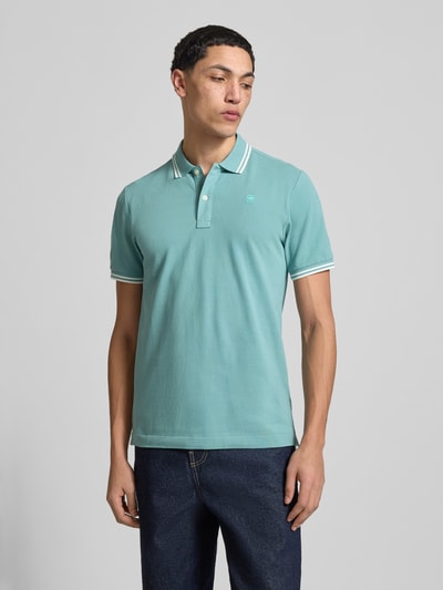 Männermodel trägt Slim Fit Poloshirt mit Logo-Stitching Modell 'Dunda' von G-Star Raw aus elastischem Baumwoll-Mix in Türkis, Polokragen, Ganzkörperansicht von vorne.