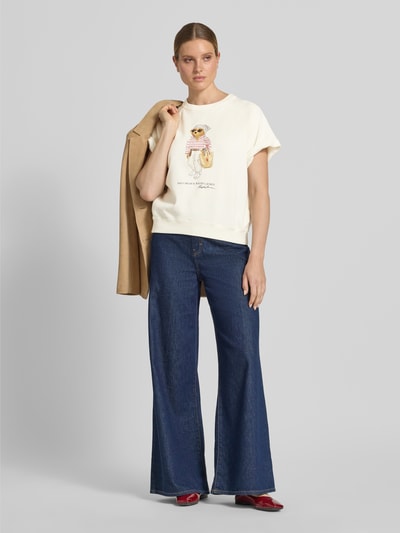 Modelka nosi Regular Fit Sweatshirt mit Polo Bear Print von Polo Ralph Lauren, efekt: jednolity kolor, krój regular fit, aplikacja: nadruk polo bear, kształt kołnierza: okrągły dekolt, rękaw: raglanowe rękawy, zakończenie rękawów: prążkowane, wykończenie materiału: dzianina dresowa, materiał: mieszanka bawełny, całkowity widok z przodu.