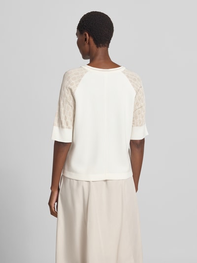 Frauenmodel trägt Relaxed Fit Bluse aus Viskose-Mix mit Allover-Logo-Detail von Marc Cain in Strick-Optik, cremefarben, Halbarm, Rundhalsausschnitt, Rückenlänge 54 cm, Ärmellänge 32 cm, Ganzkörperansicht Rückansicht.