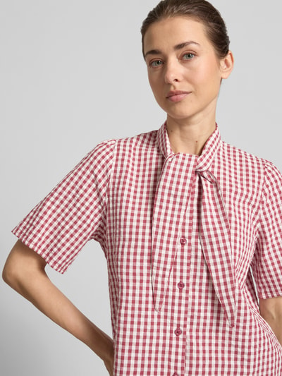 Vrouwenmodel draagt strikblouse met knoopsluiting van Jake*s Casual in rood-wit ruitpatroon, recht model, 1/2-mouwen, strikkraag, ruglengte maat 36 60 cm, mouwlengte maat 36 24 cm. Nahaufnahme oberkörper.