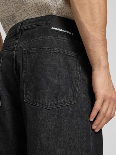 Männermodel trägt Loose Fit Jeansshorts aus Baumwoll-Mix Modell 'BAGGY' von Armedangels in schwarzer Denim-Optik mit Label Patch, Nahaufnahme Rückansicht.