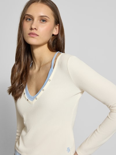 Frauenmodel trägt Slim Fit Longsleeve mit Strukturmuster von Guess Jeans in Creme mit Druckknopfbesatz und Layered-Look, Elastischer-Material-Mix, Nahaufnahme Oberkörper. Rückenlänge bei Größe S: 47 cm.