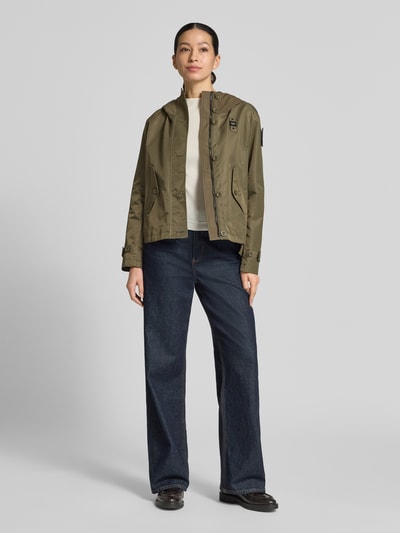 Frauenmodel trägt Regular Fit Jacke mit Logo-Detail Modell 'Marcela' von Blauer Usa in Oliv mit Kapuze und Eingrifftaschen, Ganzkörperansicht von vorne. Rückenlänge bei Größe S: 60 cm, Schulterbreite: 43 cm, Brustweite: 47 cm, Ärmellänge: 59 cm.