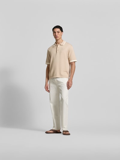 Männermodel trägt Regular Fit Poloshirt aus Baumwolle von MAISON KITSUNÉ in Beige mit Strick-Optik, Polokragen, Ganzkörperansicht von vorne.