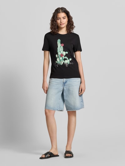 Frauenmodel trägt Damen T-Shirt Slim Fit aus reiner Baumwolle Modell 'KITA' von Only in Optik: Unifarben mit Motiv-Print und Pailletten auf Jersey, Rundhals-Ausschnitt, kurzarm, Schwarz, Ganzkörperansicht von vorne.