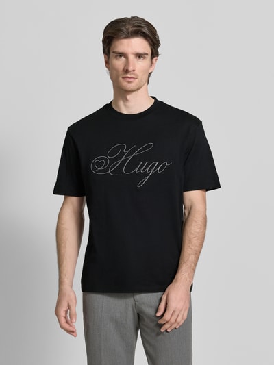 Männermodel trägt Regular Fit T-Shirt aus reiner Baumwolle Modell 'DALENT' von HUGO in Schwarz, unifarben, Label Stitching, Ganzkörperansicht von vorne.