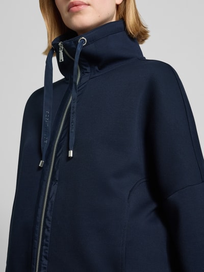 Kobiece model prezentuje Regular Fit Sweatjacke mit Viskose-Anteil od Tom Tailor, granatowa, krój regular fit, scuba, detal góry, zamek, stójka, naszywka z logo, kieszenie boczne, gładka faktura, zbliżenie na górną część tułowia.